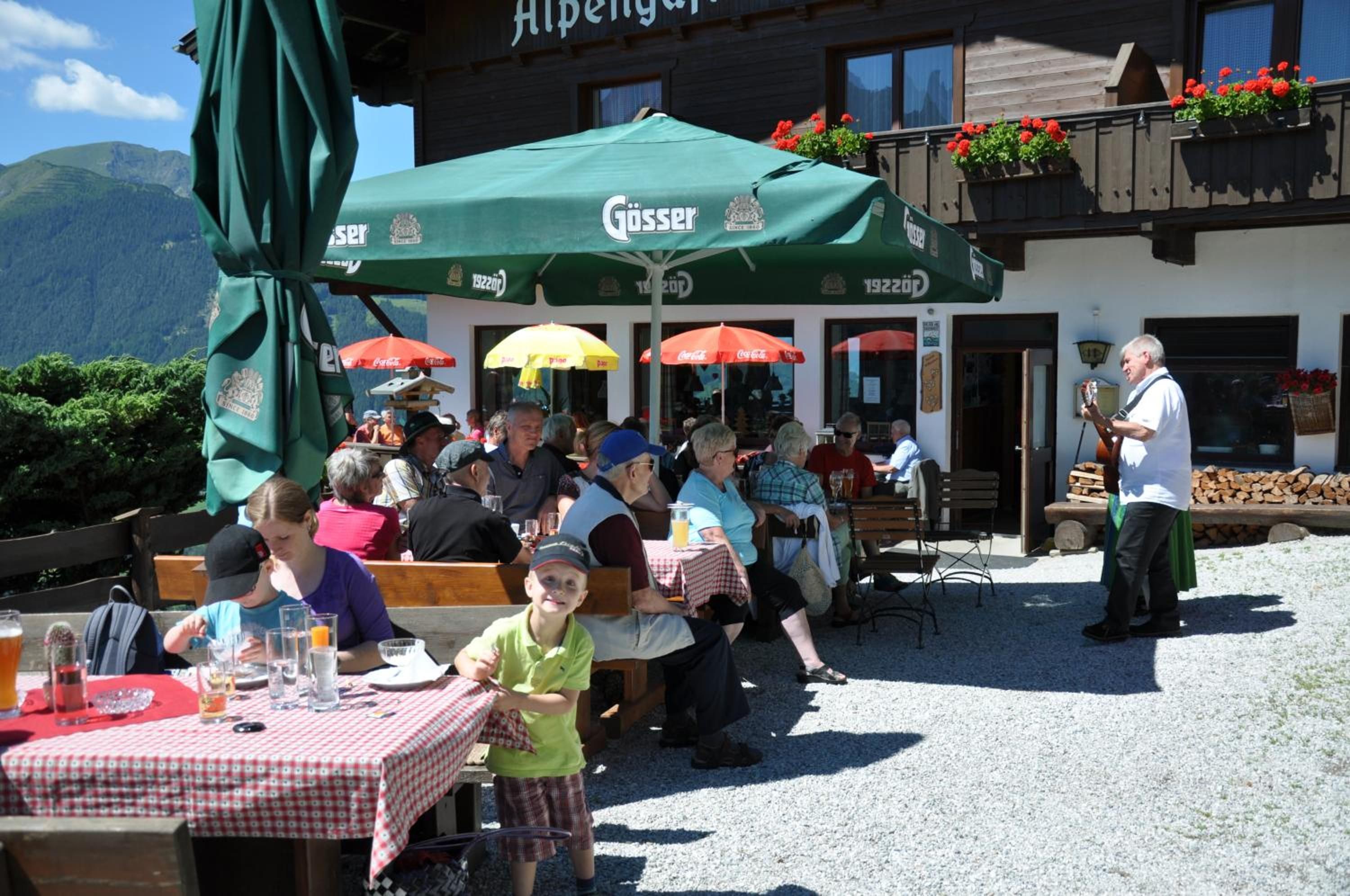 An outdoor dining area with tables and chairs, a green umbrella, and a mountain backdrop.