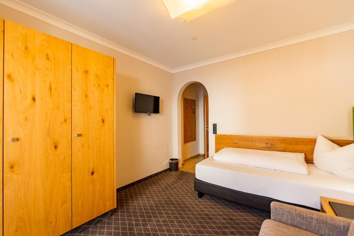 Een hotelkamer met een bed, een aan de muur bevestigde televisie en een houten garderobe.