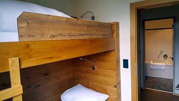 Ein Stockbett mit Holzkopfteil, einem kleinen Nachttisch und einem weißen Kissen.