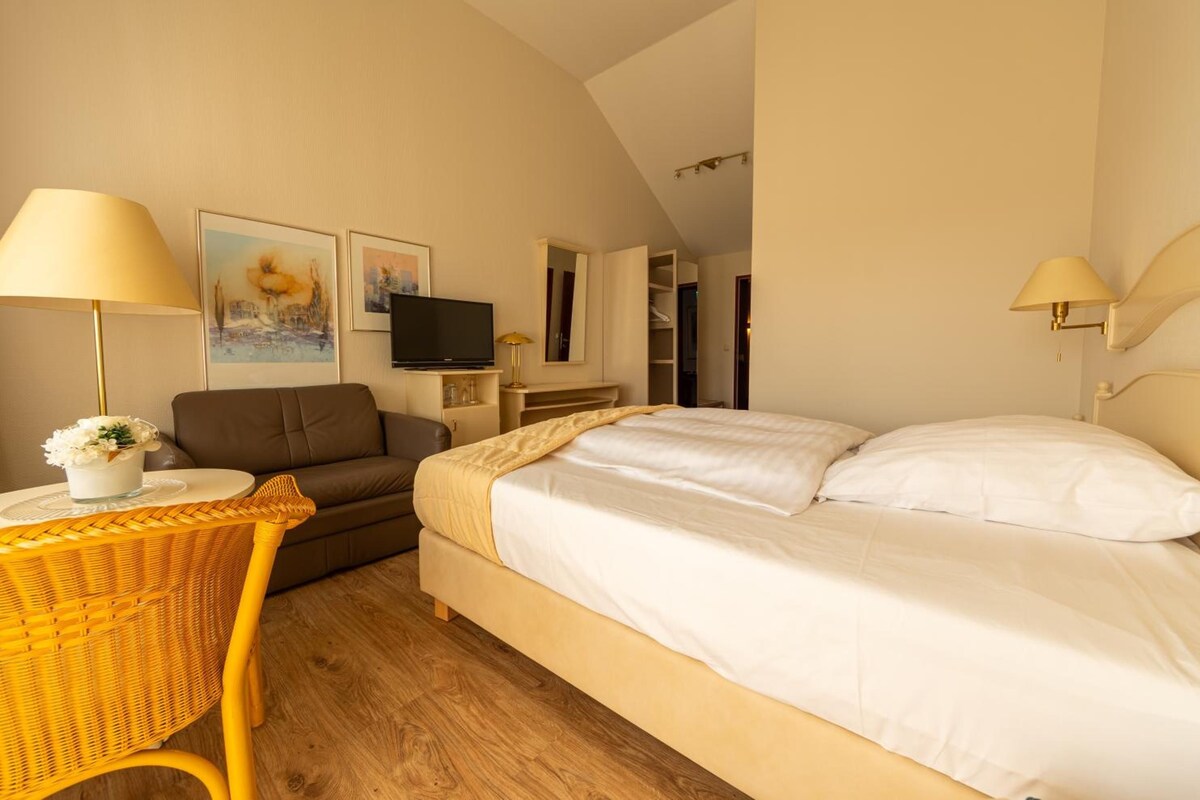 Une chambre d’hôtel comprenant un lit, une télévision, un canapé, une table avec une lampe et des œuvres d’art accrochées au mur.