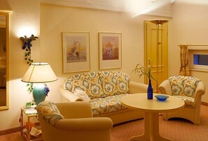 Une pièce comprenant un canapé, deux fauteuils, une petite table, une lampe et deux tableaux encadrés accrochés au mur.
