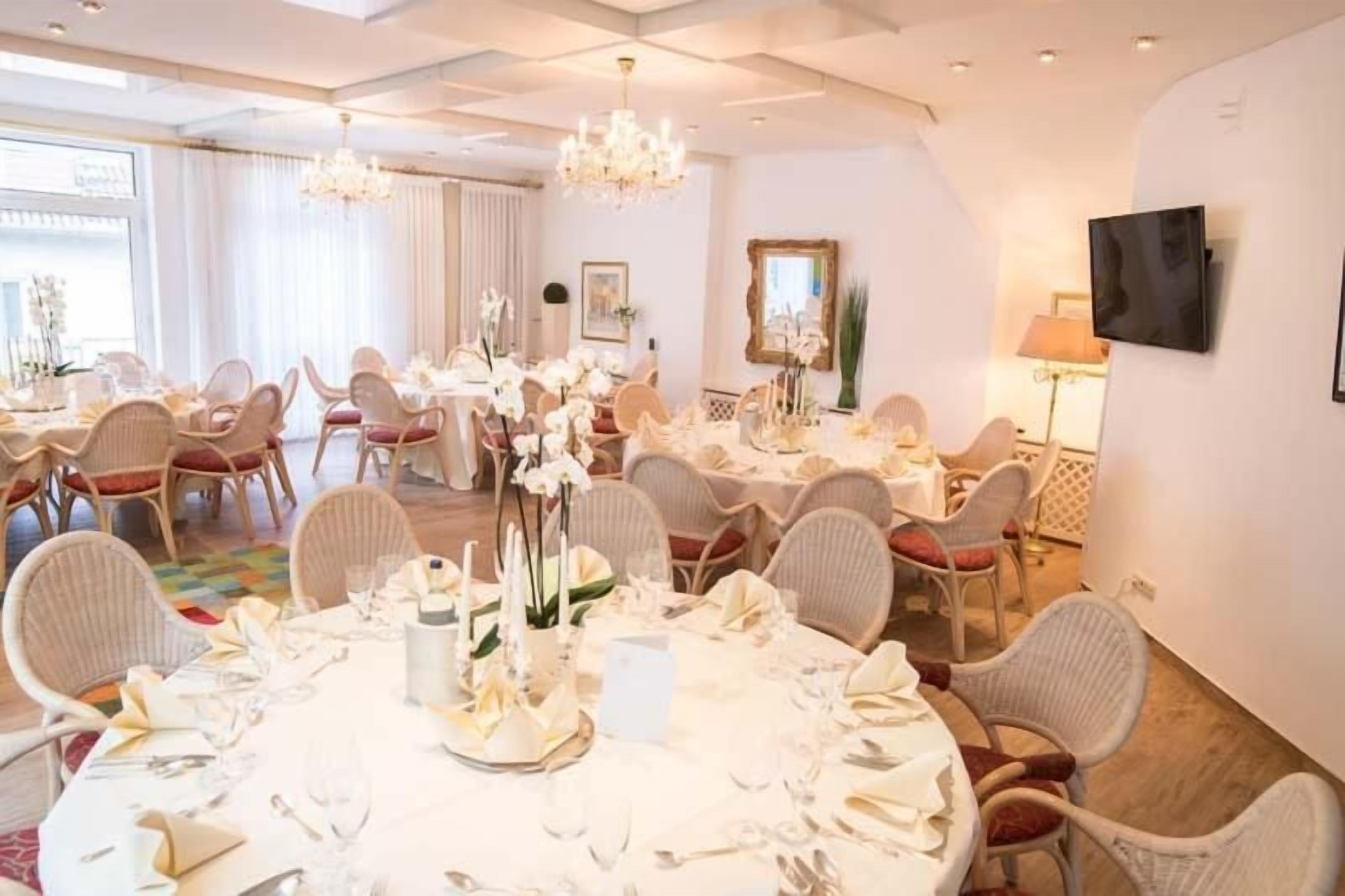 A dining area with round tables set for a meal, surrounded by wicker chairs.