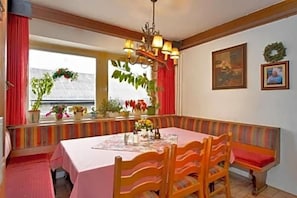 Un comedor con mesa, sillas, un banco y una ventana con cortinas.
