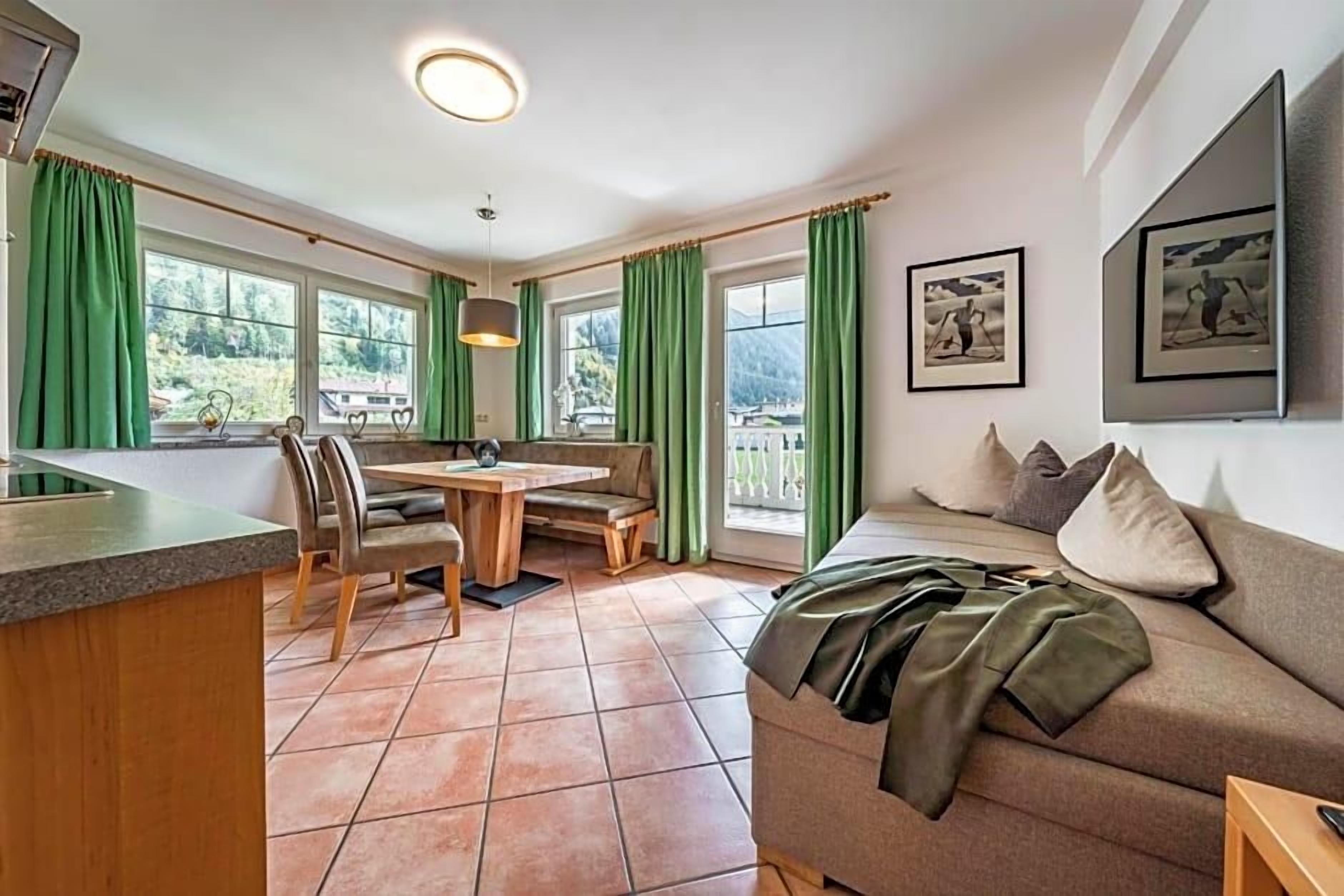 A room with a dining table, chairs, a sofa, and a kitchen counter.