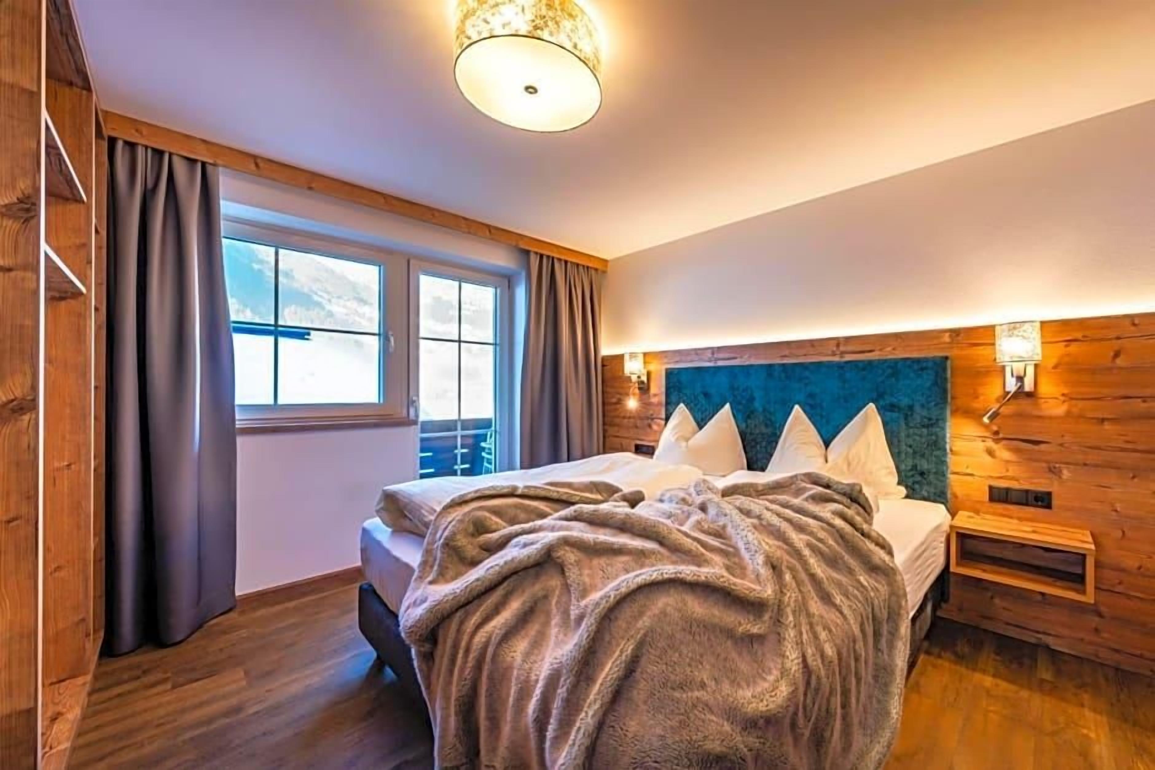 A bedroom with a bed, a window, wooden walls, and a ceiling light.