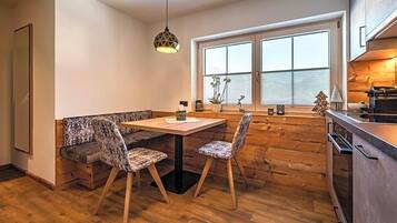 A modern kitchen with a wooden bench, two chairs, a hanging light fixture, and a window with blinds.