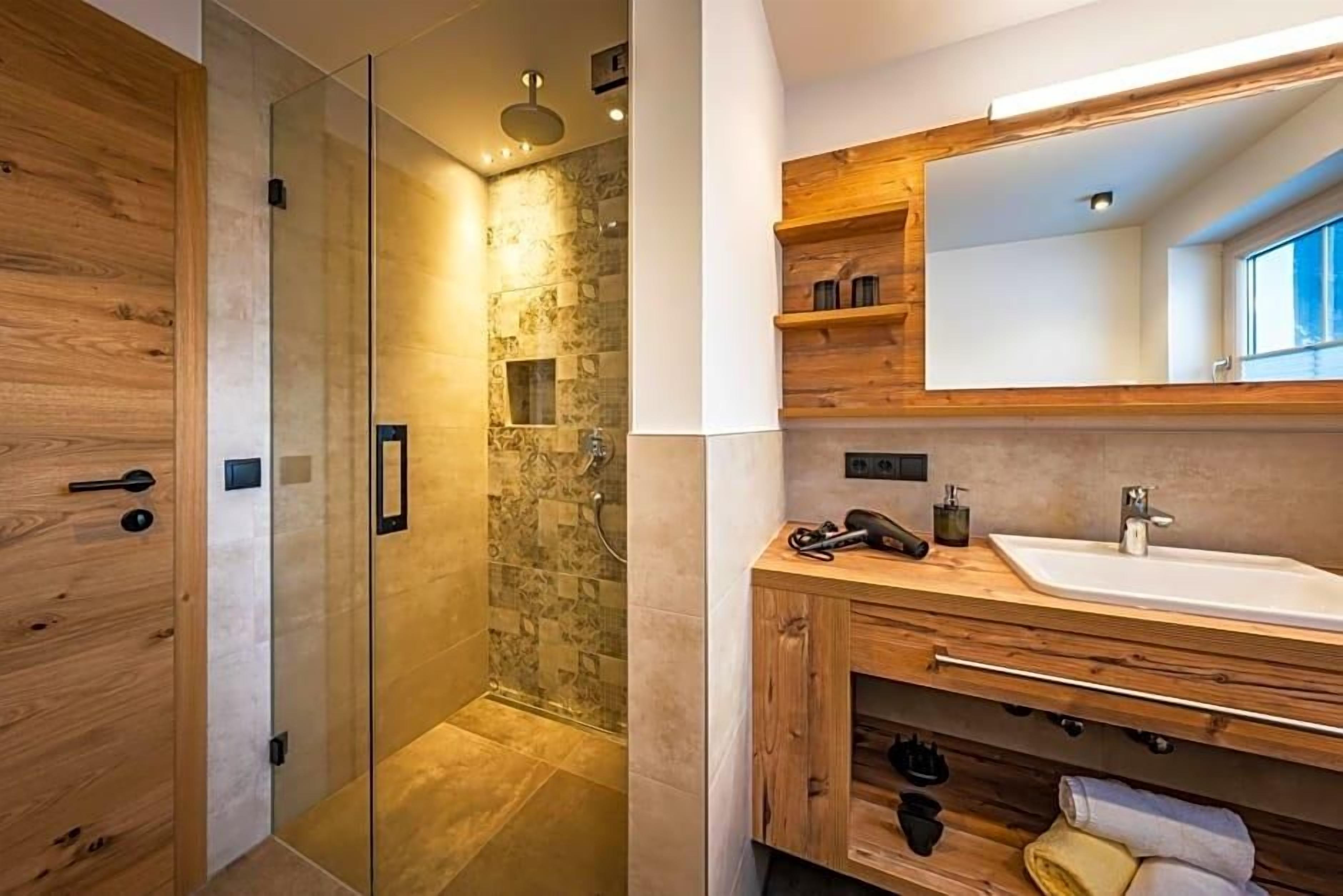 A modern bathroom with a glass-enclosed shower, wooden cabinetry, and a large mirror above the sink.