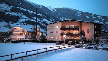 A hotel with a snow-covered landscape, multiple floors, and a mountain backdrop.