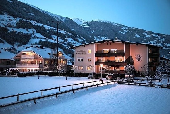 A hotel with a snow-covered landscape, multiple floors, and a mountain backdrop. - Haus Wiesengrund (Mayrhofen)