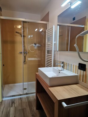 A modern bathroom with a glass-enclosed shower, a white sink, and a wooden vanity.