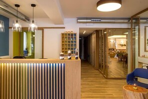 A reception area with a wooden reception desk, pendant lighting, and a glass partition leading to a dining area.