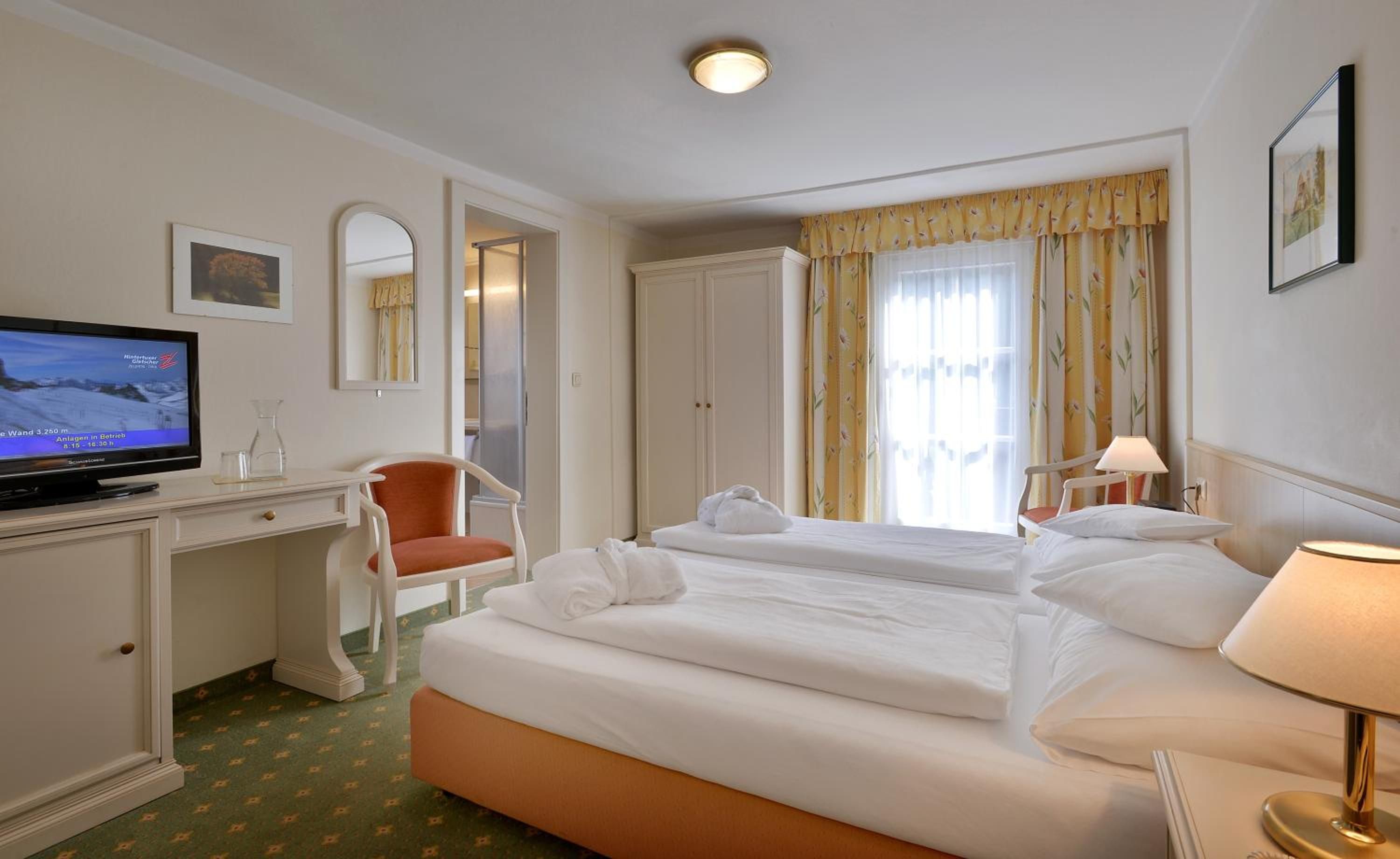 Une chambre d’hôtel avec un lit, un bureau avec une télévision, une chaise et une fenêtre avec des rideaux.