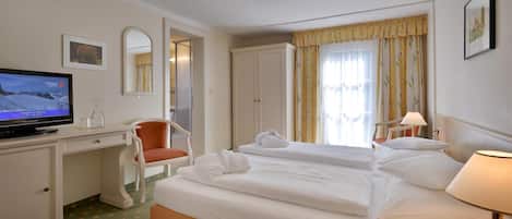A hotel room with a bed, a desk with a television, a chair, and a window with curtains.