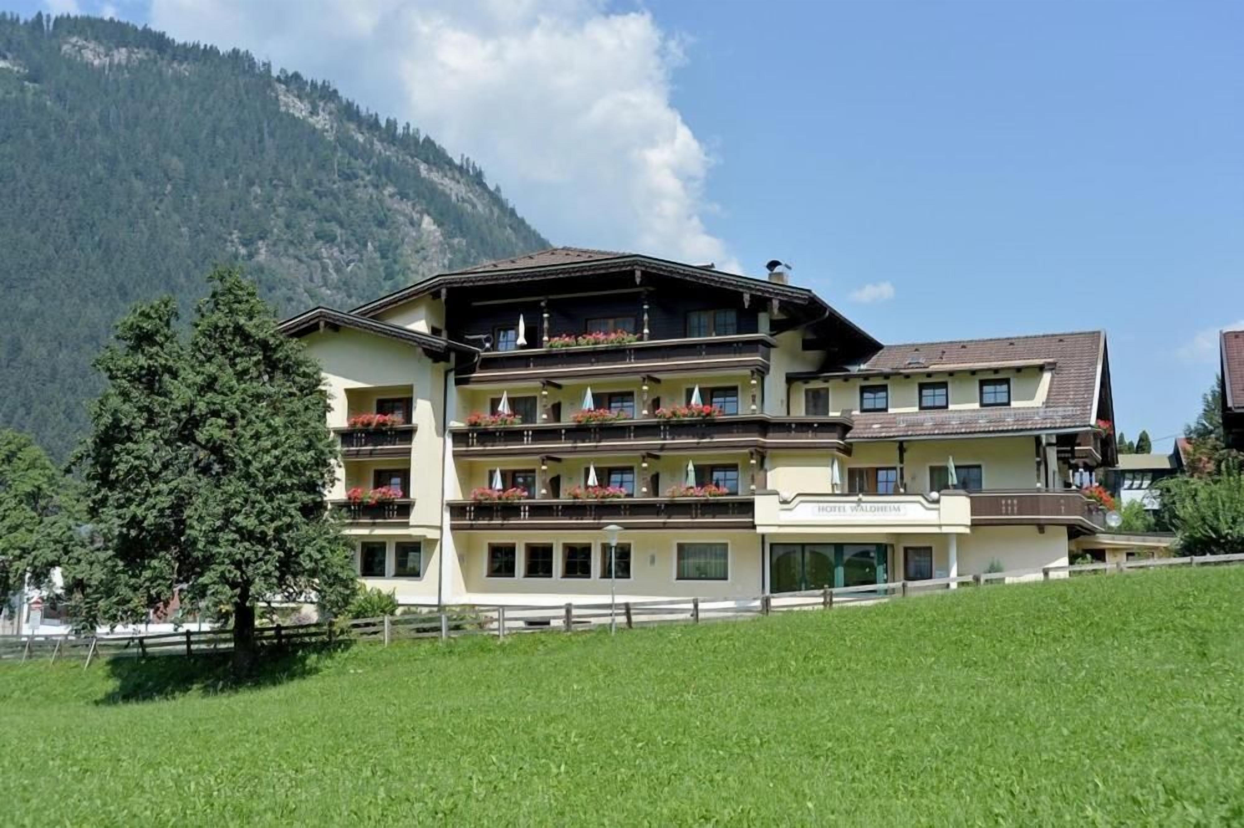 A multi-story hotel with balconies, set against a mountainous backdrop.