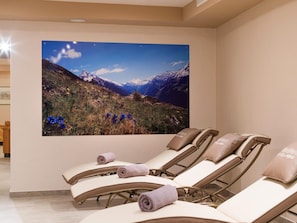 A room with reclining chairs, a large wall-mounted picture of a mountainous landscape, and a wooden side table. - Waldheim (Mayrhofen)