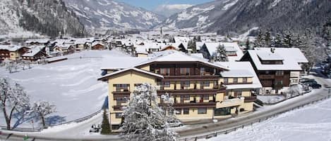 Un pueblo nevado en la montaña con edificios de madera tradicionales, una pista de esquí y cielo despejado.