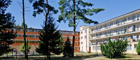 Un edificio de varios pisos con techo plano, rodeado de árboles y un área verde.