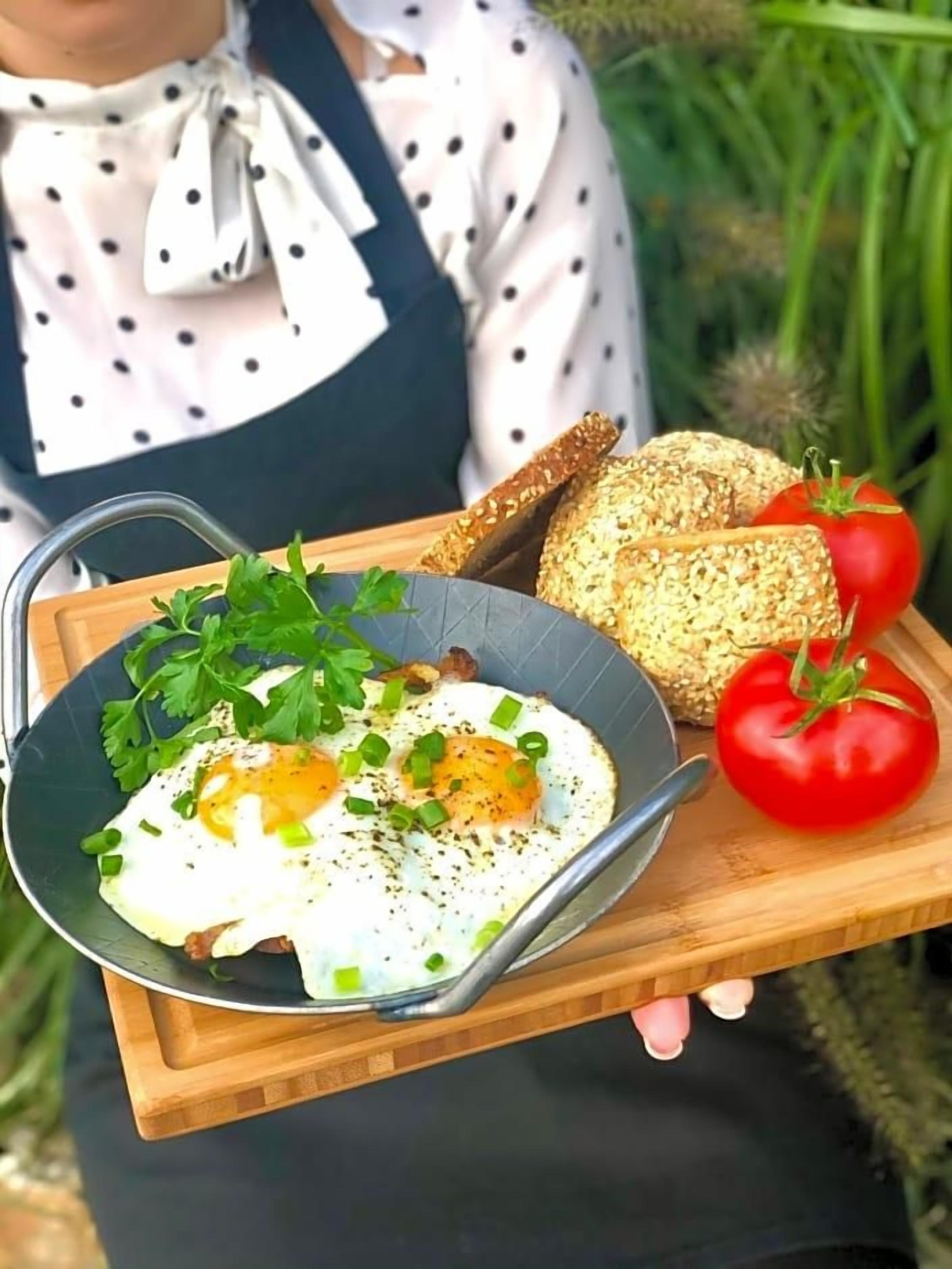 A person holding a tray with a plate of eggs, bread, and tomatoes.