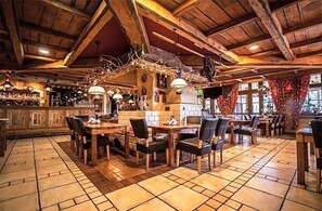 A restaurant with wooden tables and chairs, a bar area, and a fireplace. - Korona (Klodzko Miasto)