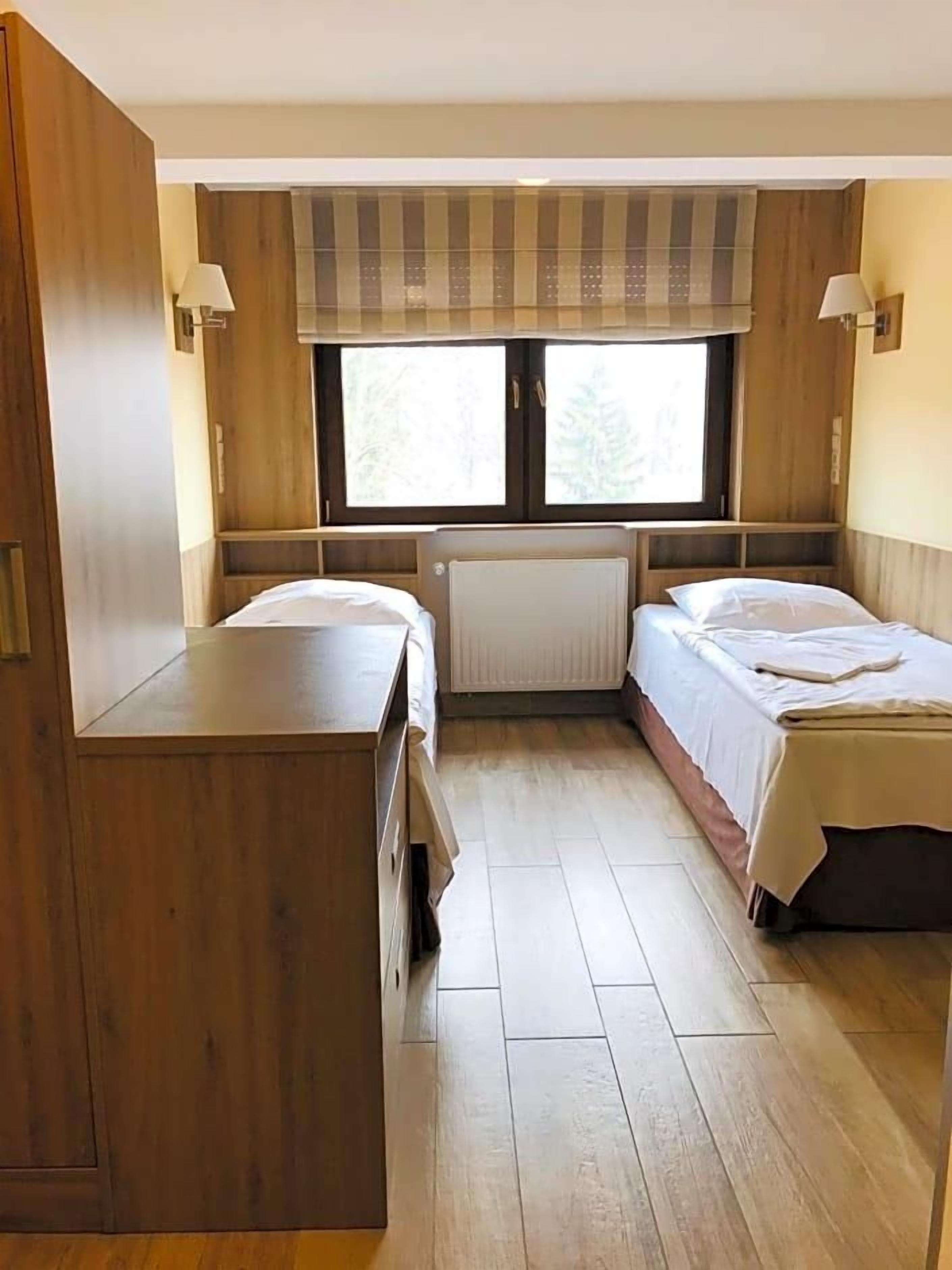 A compact room with two beds, a wooden desk, and a window with curtains.