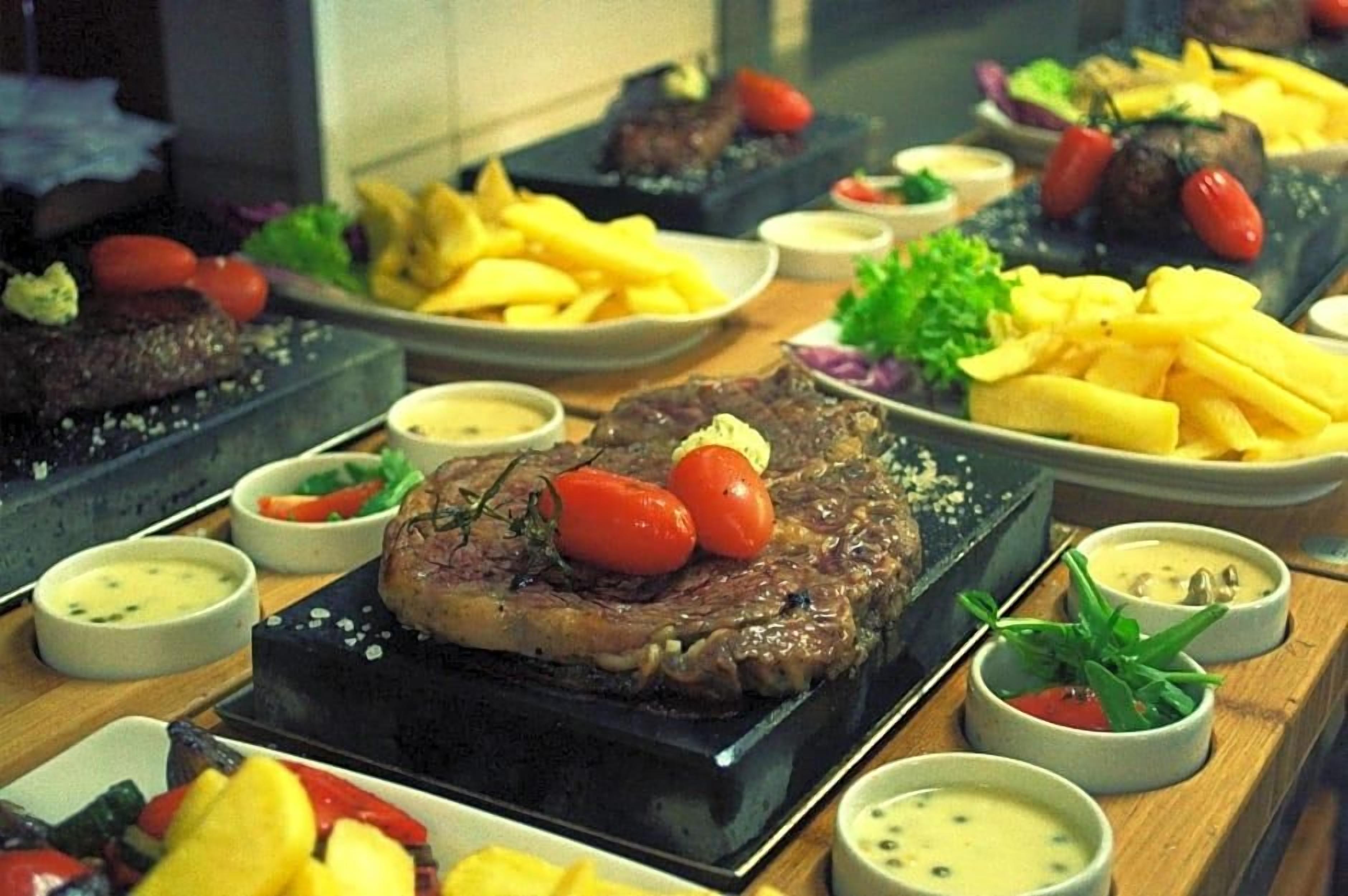 A dining table with multiple plates of food, including steak, fries, and various side dishes.