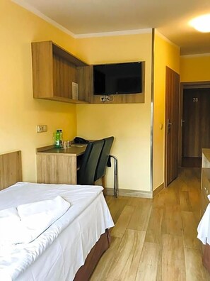 A hotel room with a bed, a desk, a chair, a TV mounted on the wall, and a wardrobe. - Korona (Klodzko Miasto)