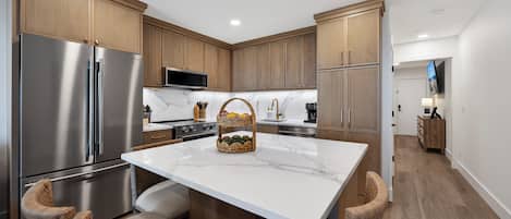 A modern kitchen with a stainless steel refrigerator, wooden cabinets, a marble countertop, and a built-in oven.
