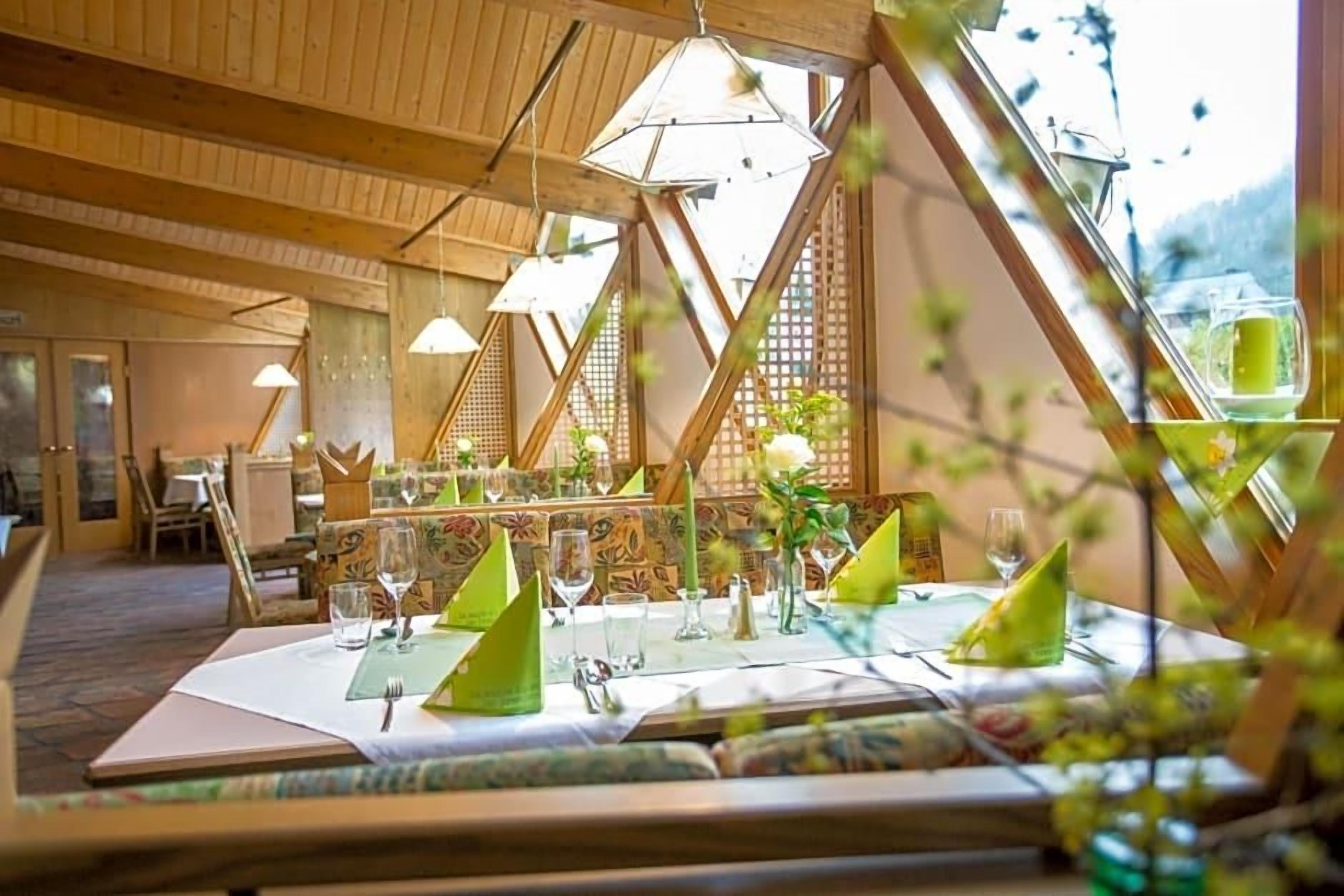 Un comedor con mesas dispuestas para dos personas, con detalles de madera y luz natural que entra por amplias ventanas.