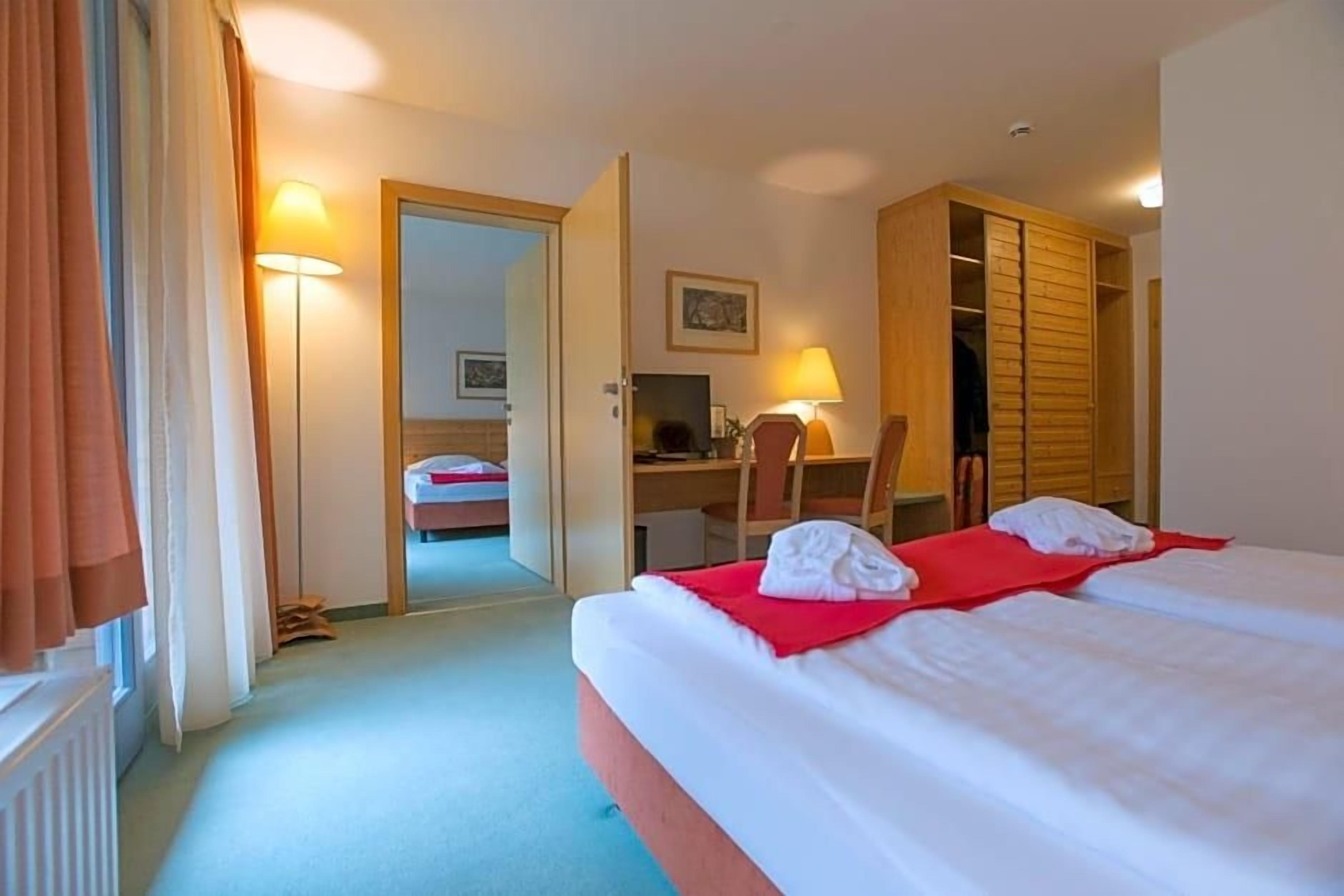 Habitación de hotel con cama, escritorio, silla, armario y puerta que da a otra habitación.