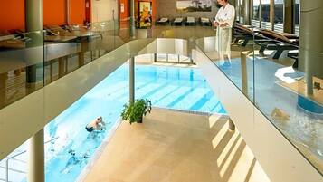 Une piscine dotée d’une barrière en verre, une personne dans l’eau et une autre personne debout au bord de la piscine.