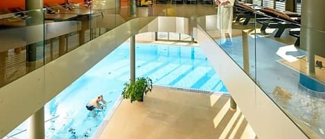 Una piscina con barandilla de vidrio, una persona en el agua y otra de pie junto a la piscina.