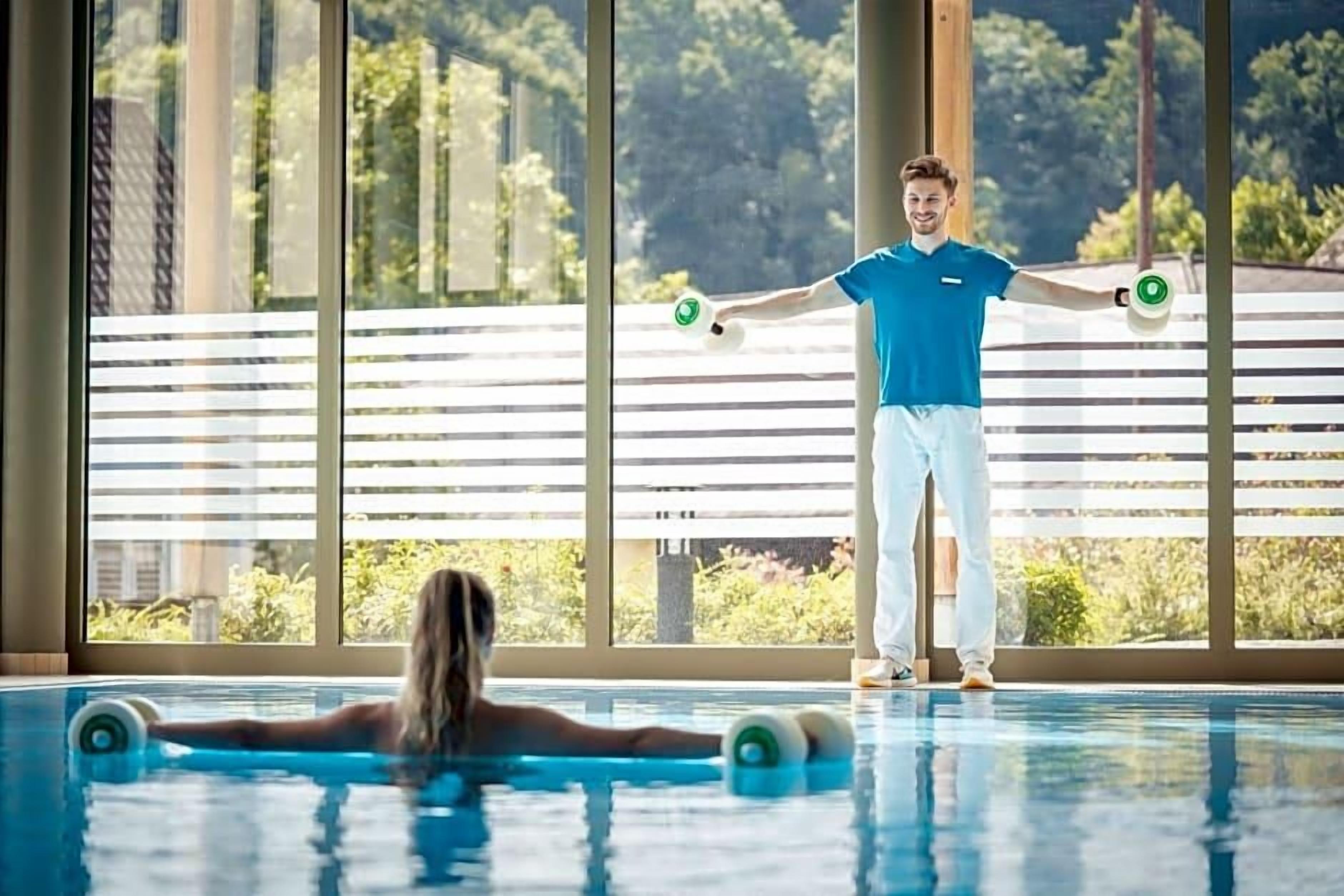 Una persona de pie en una piscina, con vista a un edificio y follaje exterior.