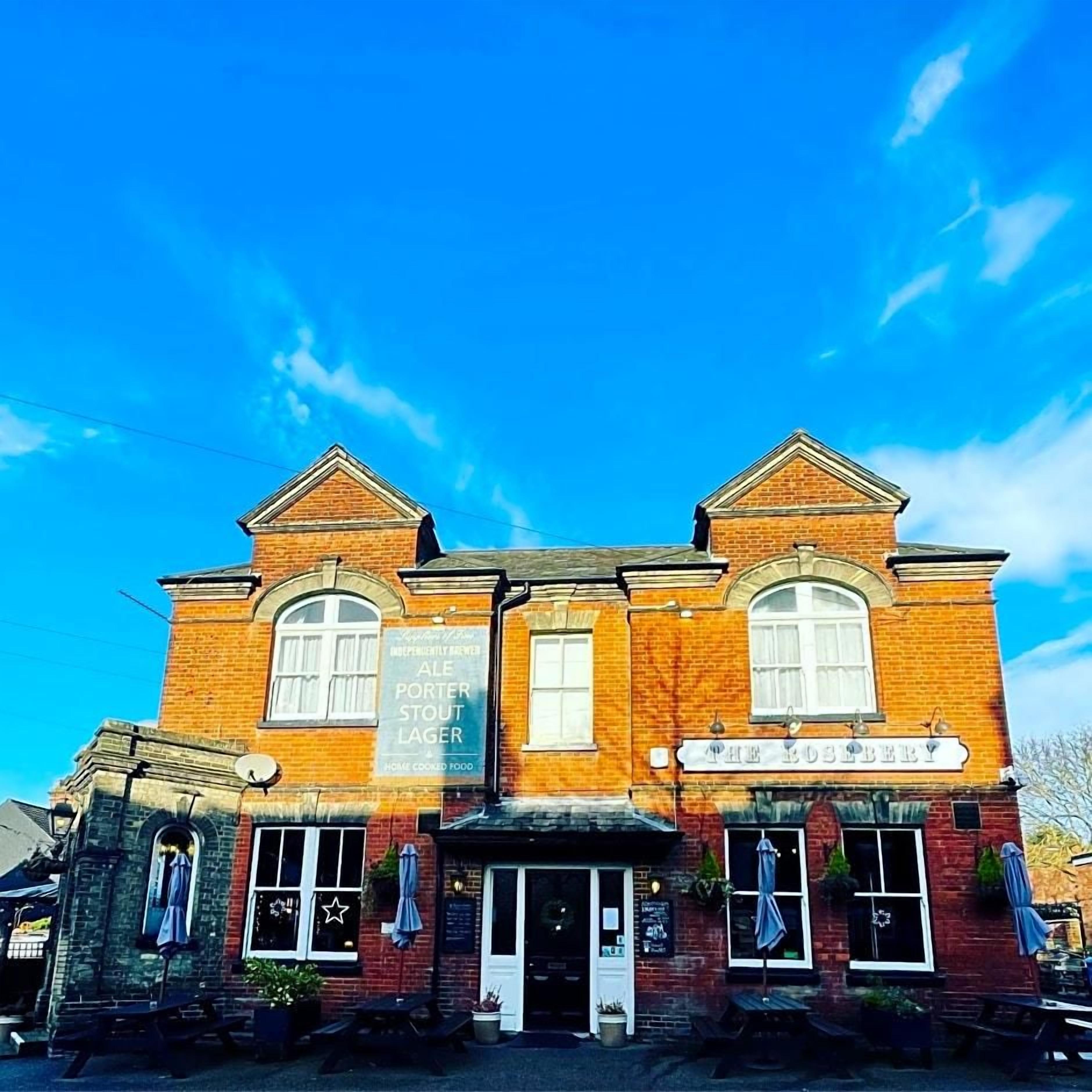 A brick building with a sign for 'The Rosebery' and another sign advertising 'ALE PORTER STOUT LAGER HOME COOKED FOOD.'