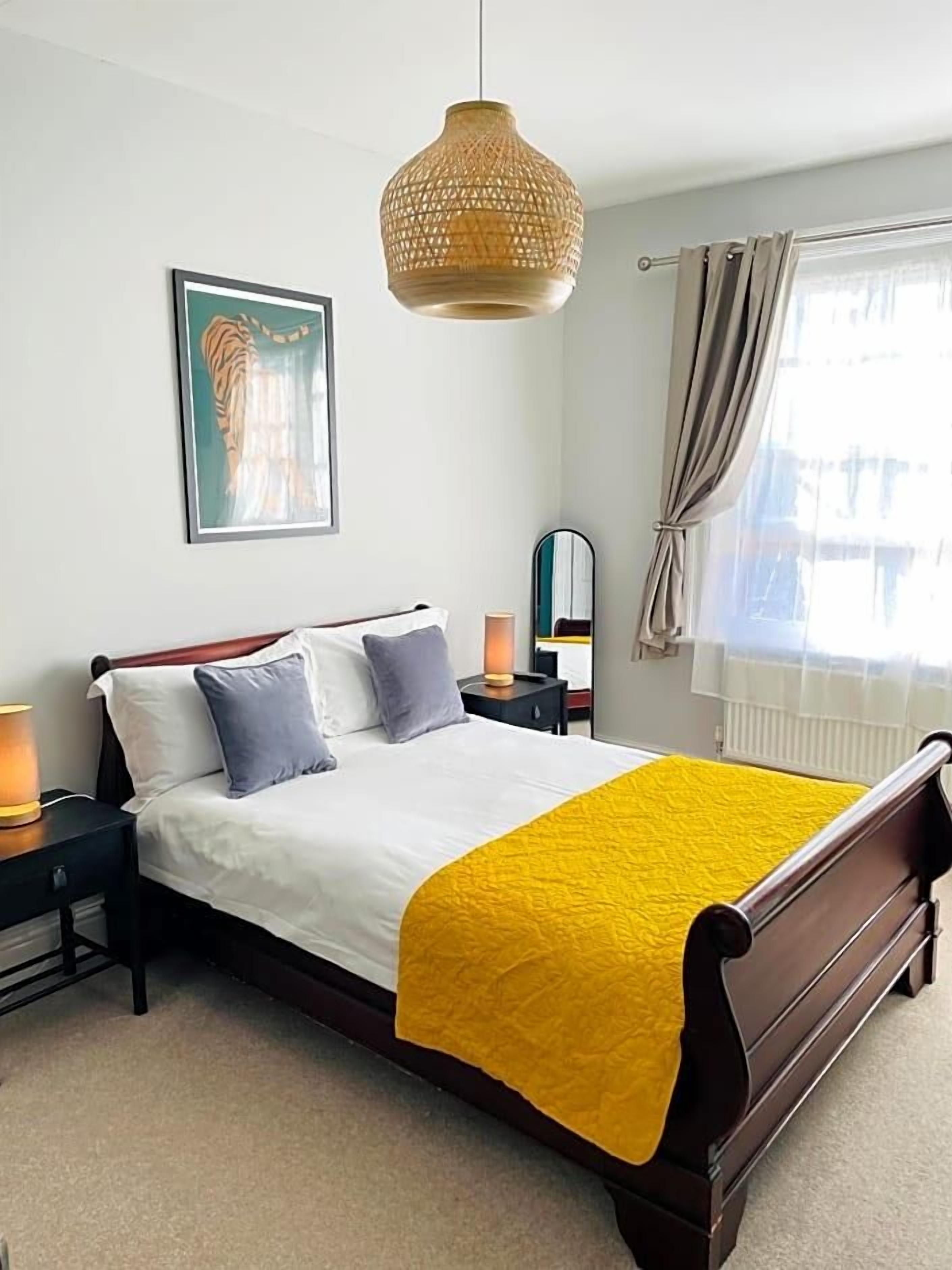 A neatly made bed with a white comforter and a yellow throw blanket, a bedside lamp, and a framed picture on the wall.