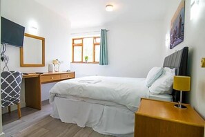 A bedroom with a bed, bedside table, lamp, and a window with curtains. - The Residence Jaipur (York)
