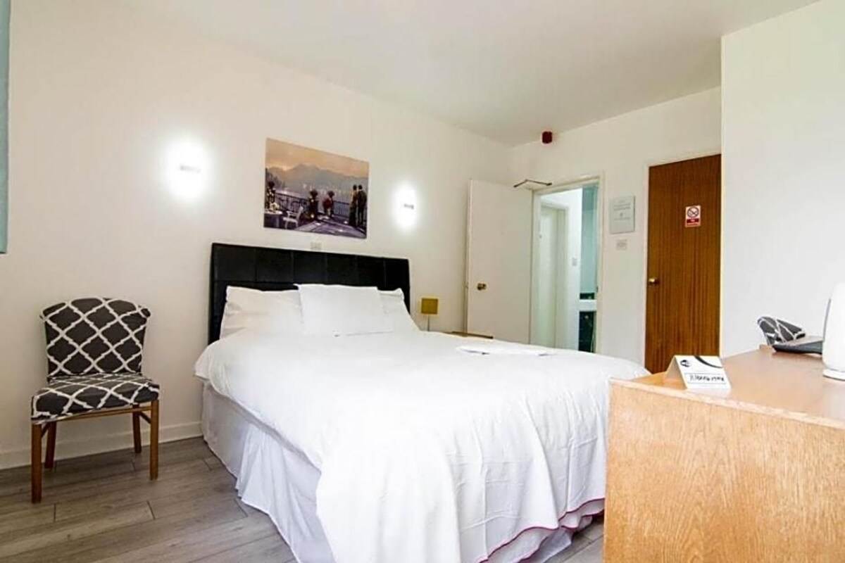 A hotel room with a bed, a chair, a desk, and a door.