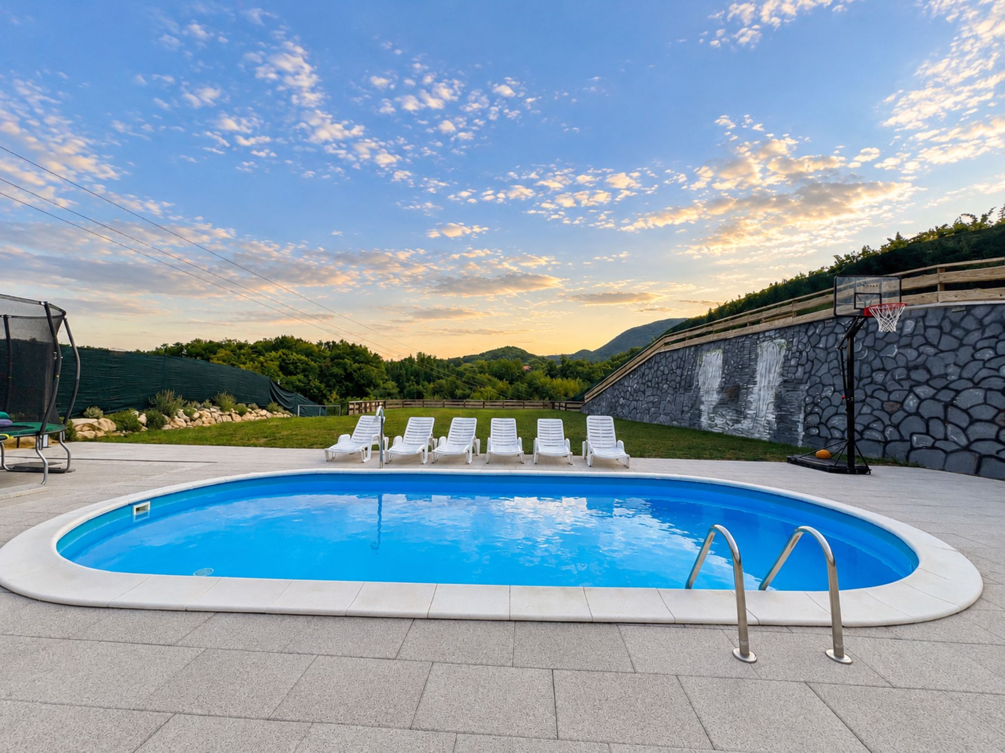 A swimming pool with a stone wall and a basketball hoop.