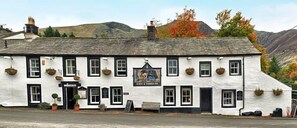 Un edificio blanco con detalles negros, un cartel que dice 'Horse & Hound Inn' y un telón de fondo de montañas.