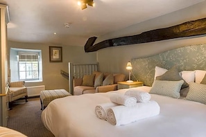 Una habitación de hotel con una cama grande, una zona de estar con una silla y una mesita, y una ventana con persianas.