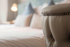 Primer plano de una cama con cabecera, almohadas y una lámpara de noche.