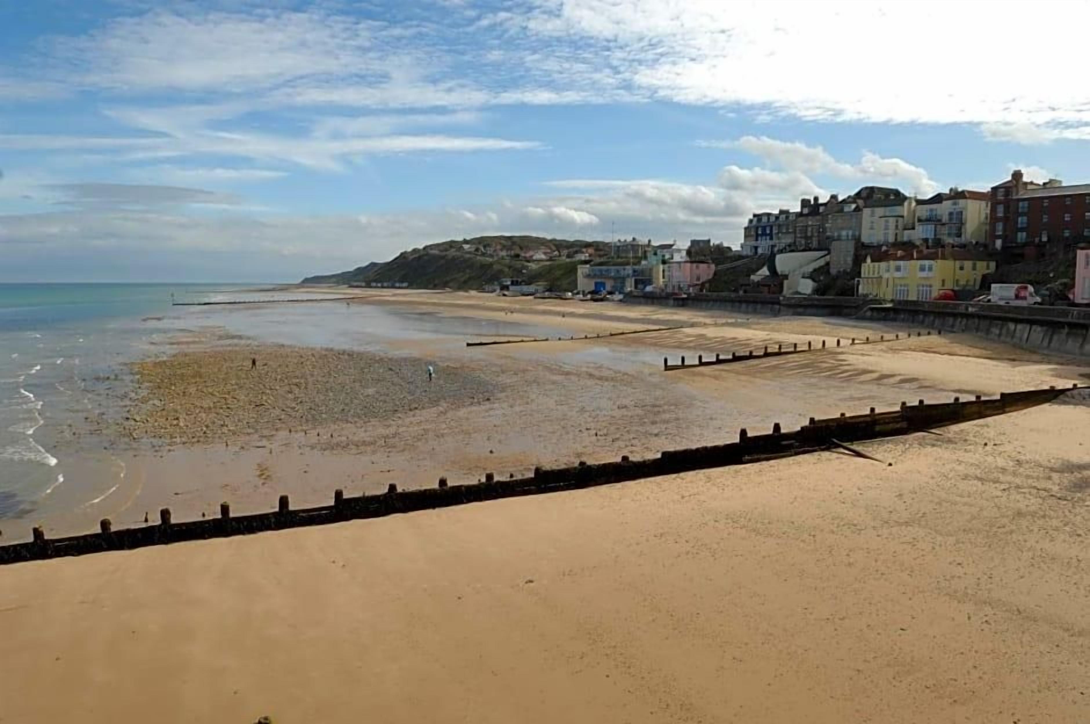 A beach with a sandy shore, a wooden barrier, and buildings in the background.