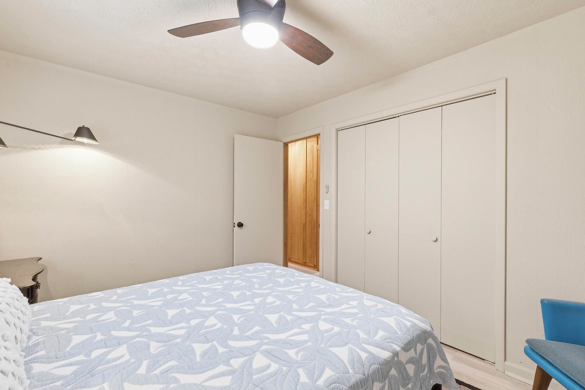 Une chambre à coucher comprenant un lit, un ventilateur de plafond, une armoire et une table de chevet.
