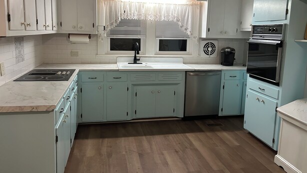 Cocina con gabinetes blancos, un lavamanos, una estufa y un lavavajillas.