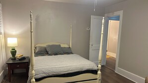 Una cama con dosel con un edredón gris, una mesita de noche con una lámpara y una alfombra estampada.