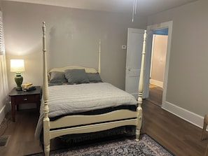Una cama con dosel con un edredón gris, una mesita de noche con una lámpara y una alfombra estampada.
