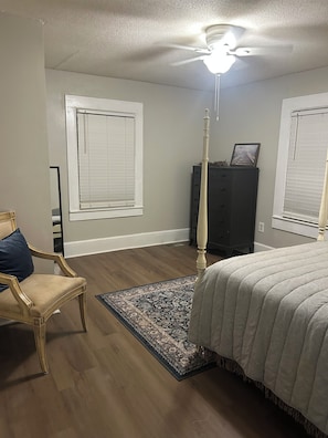 Un dormitorio con cama, una silla, cómoda y ventilador de techo.