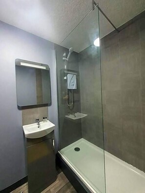 Une salle de bain moderne avec une douche à parois de verre, un lavabo sur colonne et un miroir fixé au mur.