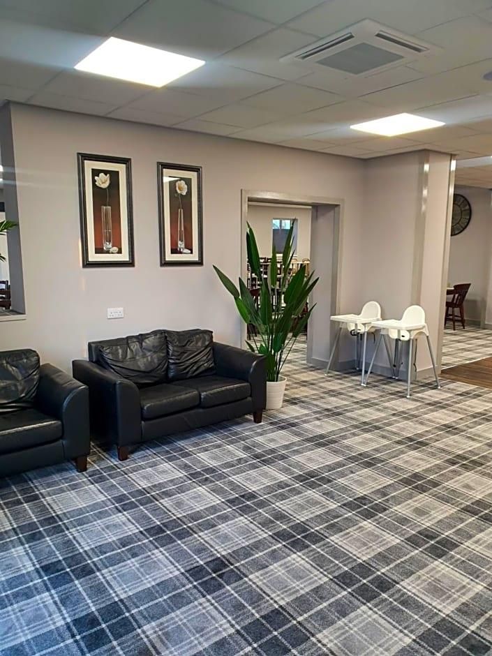 A lobby with a checkered floor, a black leather sofa, two framed pictures, a potted plant, and a small table with chairs.