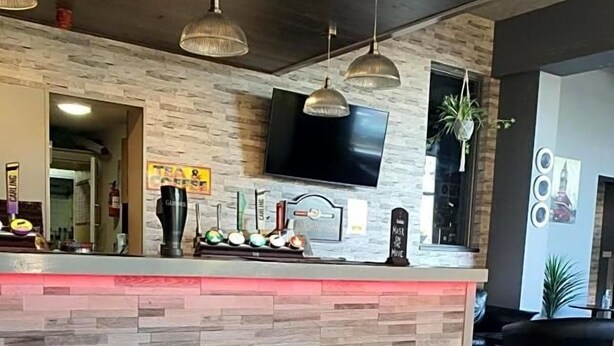 A reception area with a stone-textured counter, pendant lighting, a flat-screen TV, and a seating area with a black sofa. - Harleys Inn (Chesterfield)
