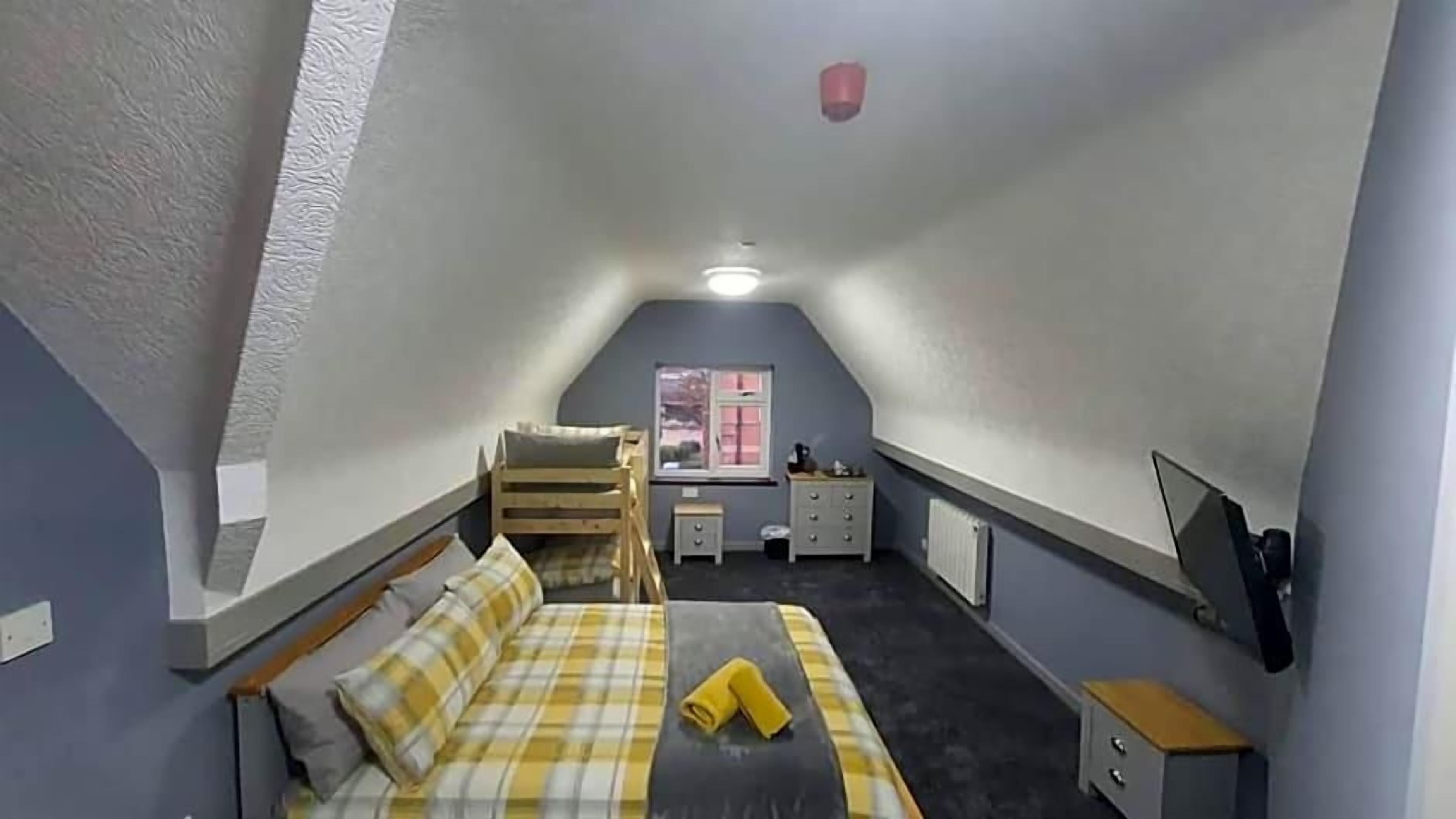 A small, sloped-roofed room with a bed, a desk, a chair, and a window.